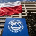MFW Polska wzrost gospodarczy – polska flaga na tle siedziby Międzynarodowego Funduszu Walutowego, ilustracja do tekstu o prognozach wzrostu gospodarczego Polski i Europy.